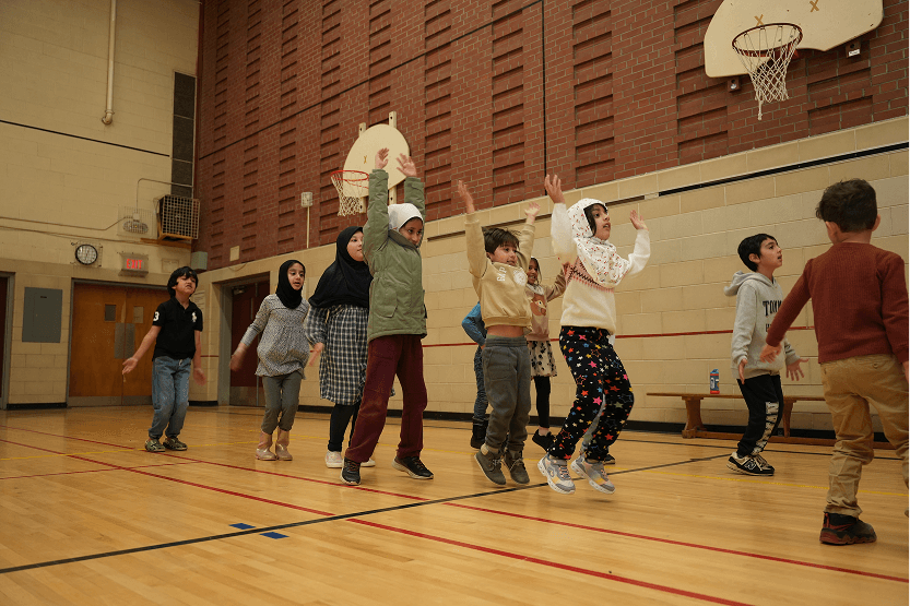 Group of children playing and jumping inside a gymnasium near basketball hoops.